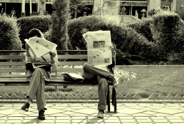 Old timey picture of people sitting on the park bench reading newspapers